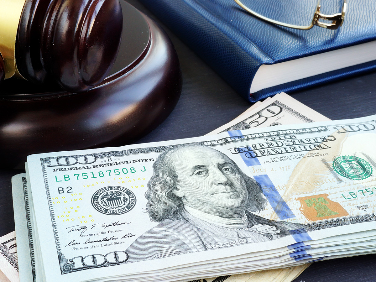 Hundred dollar bills stacked on a desk next to a gavel. 