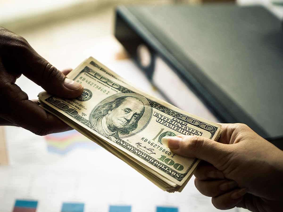 a person handing over a stack of 100 dollar bills