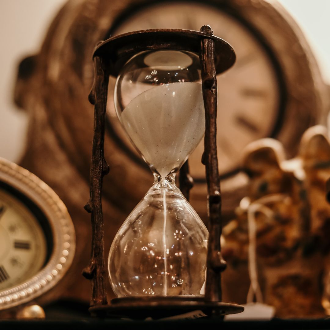 Hourglass with sand, antique clocks in background